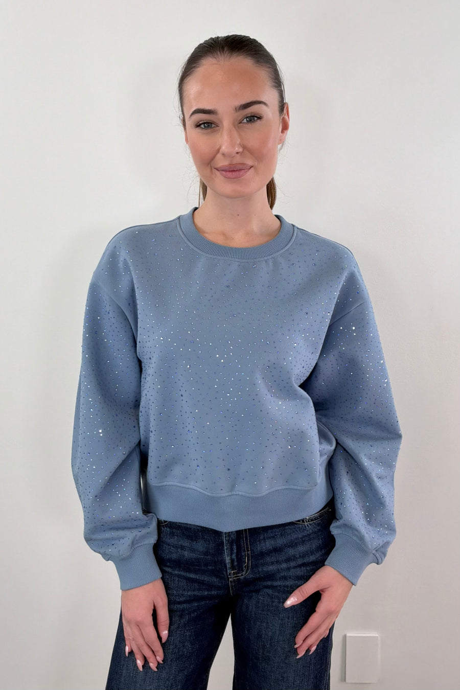 Woman wearing blue pullover with rhinestone details all over