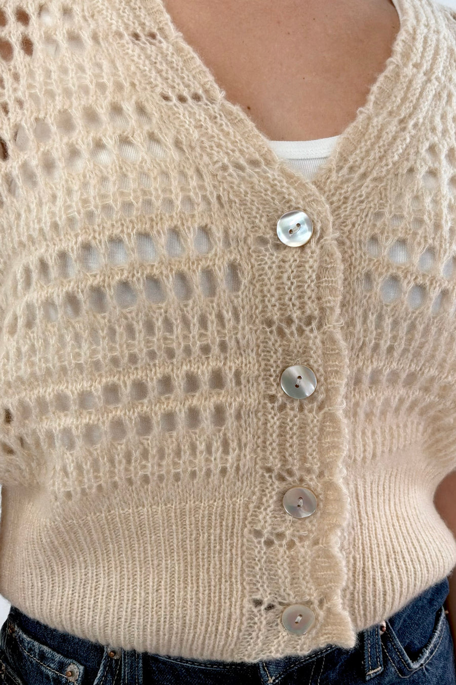 Close up of a woman wearing a pointelle knit cardigan in latte with pearl white buttons