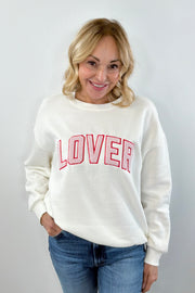 A woman wearing an off white crewneck sweatshirt with the word  “LOVER” written in pink chenille