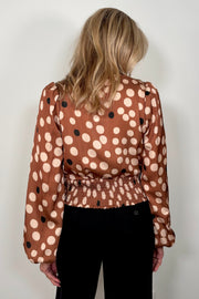 Back view of woman wearing a dusty warm brown top with bicolored dots, soft puff sleeves and wrap front