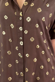 Close up of woman wearing a brown short shirt dress with gold detailing
