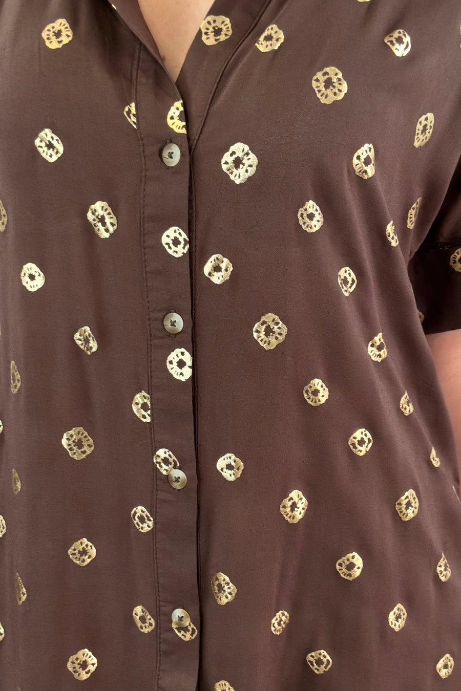Close up of woman wearing a brown short shirt dress with gold detailing