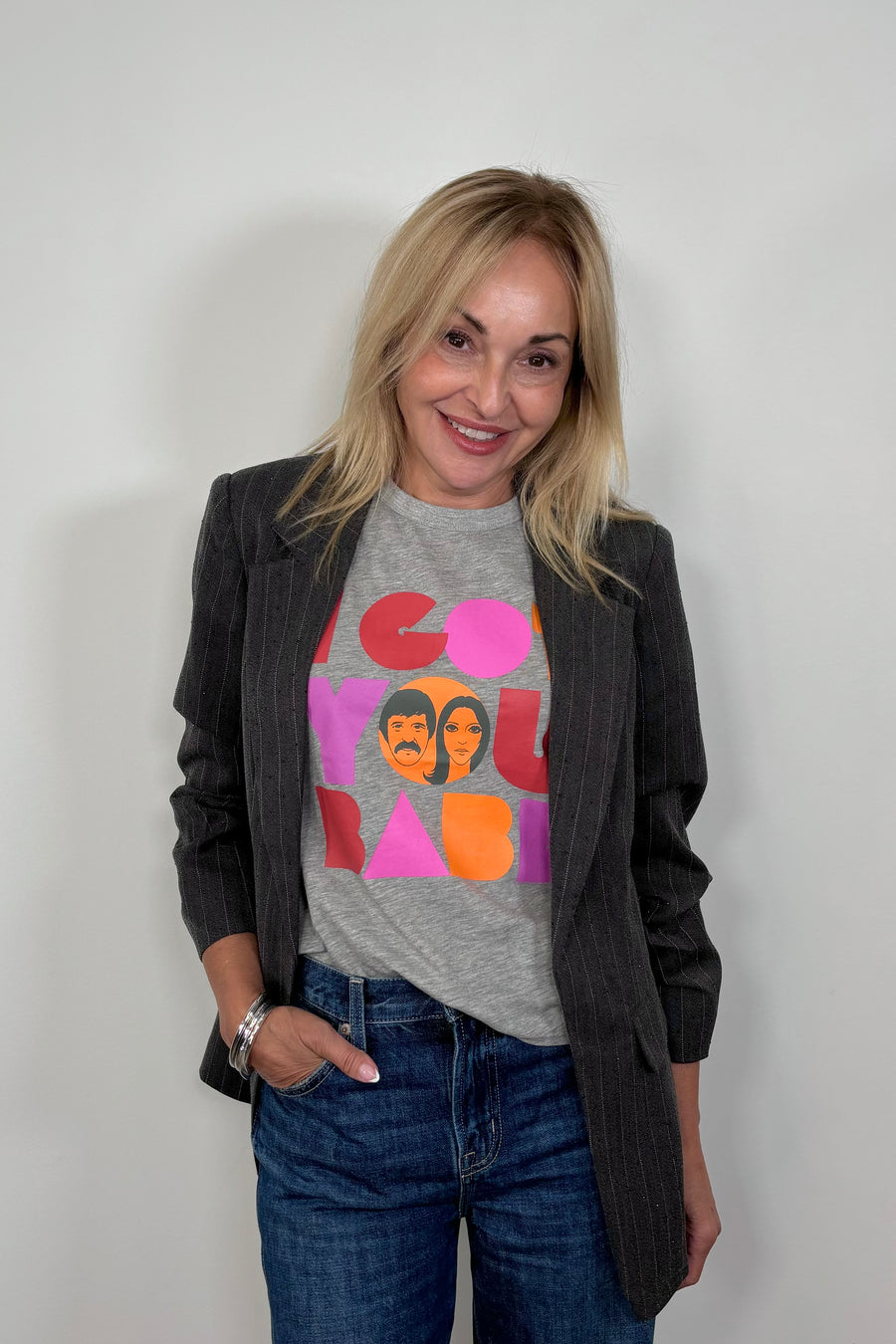 Front facing woman wearing a gray sleeveless tee with “I got you babe” graphic words printed paired with a dark gray blazer with rhinestones