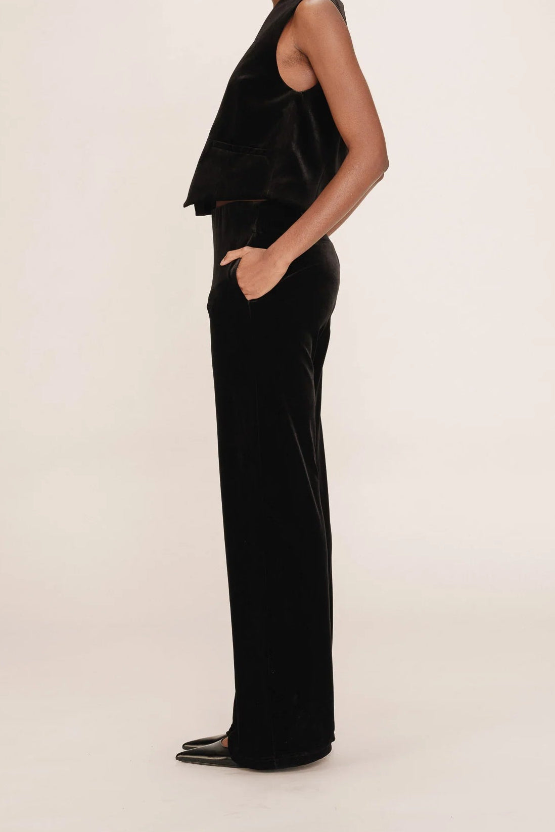 Woman wearing a black sleeveless top and high-waisted pants against a white background