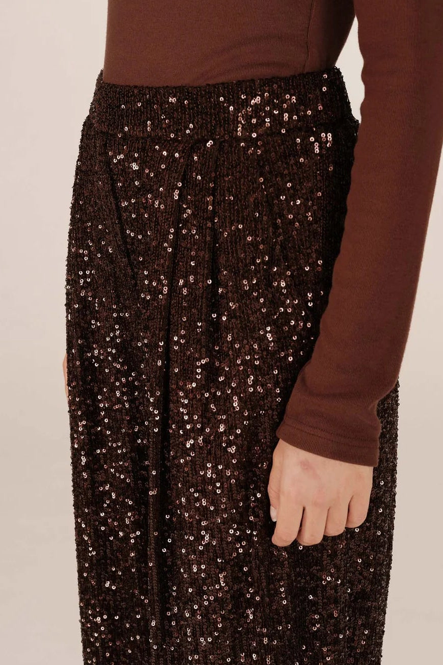 Person wearing a brown sequined skirt and brown top on a beige background