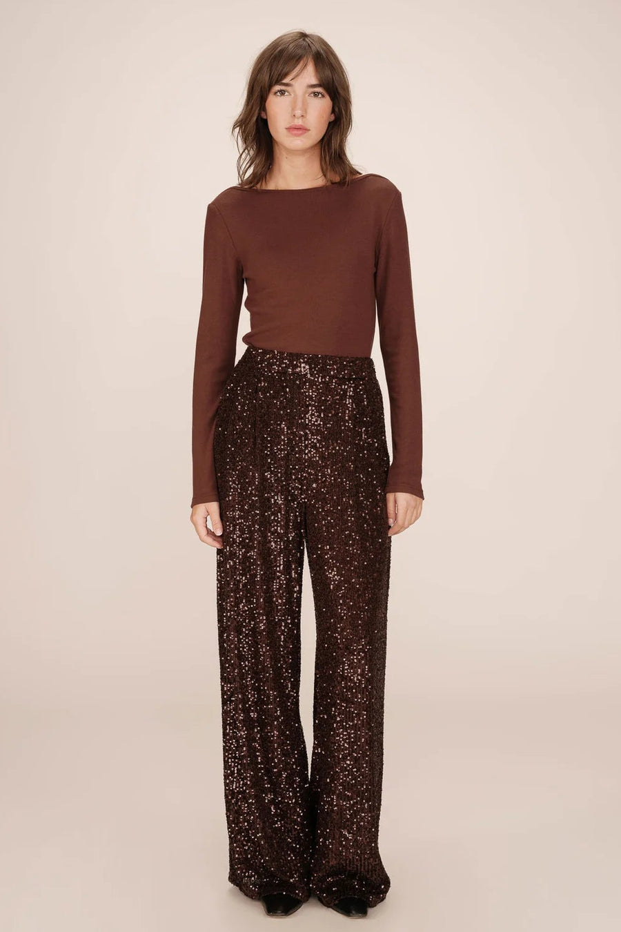 Woman wearing a brown long-sleeve top and patterned pants on a beige background