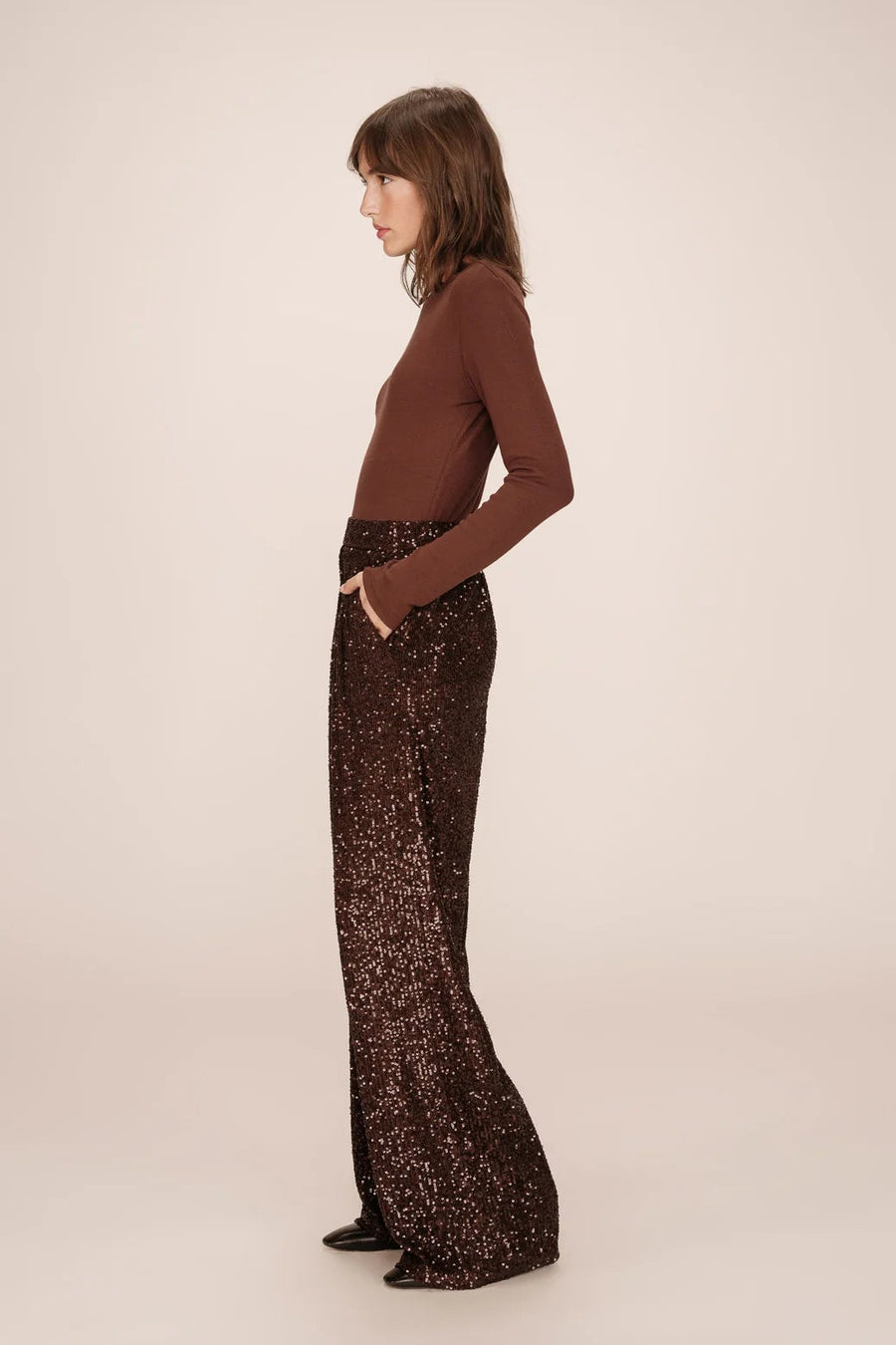Woman wearing a brown top and black patterned pants on a beige background