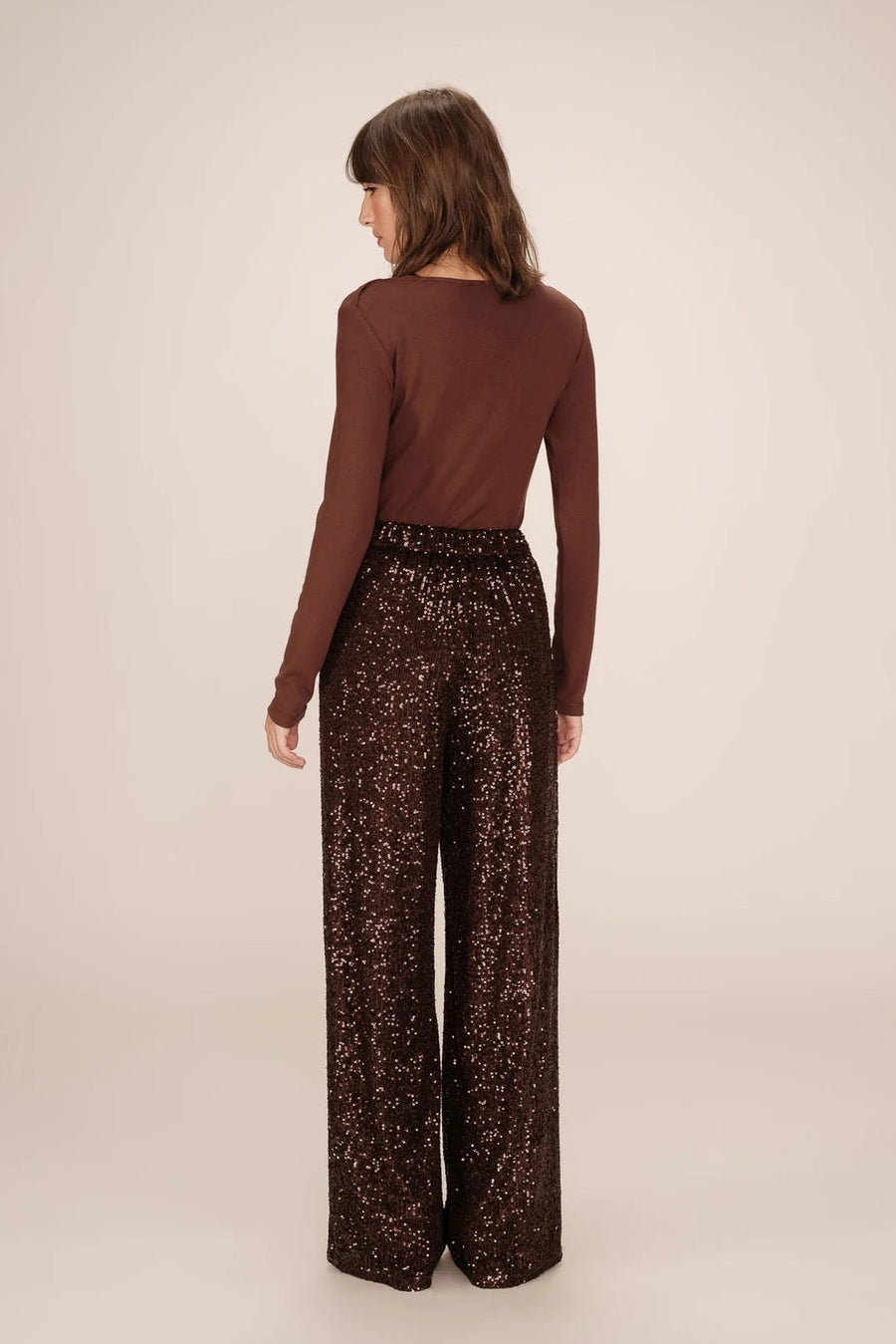 Woman wearing a brown long-sleeve top and patterned pants on a beige background