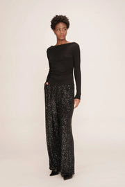 Person wearing a black one-shoulder top and patterned pants on a white background