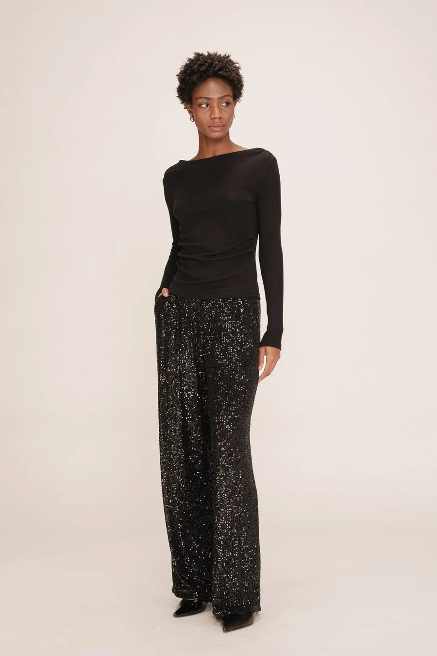 Person wearing a black one-shoulder top and patterned pants on a white background