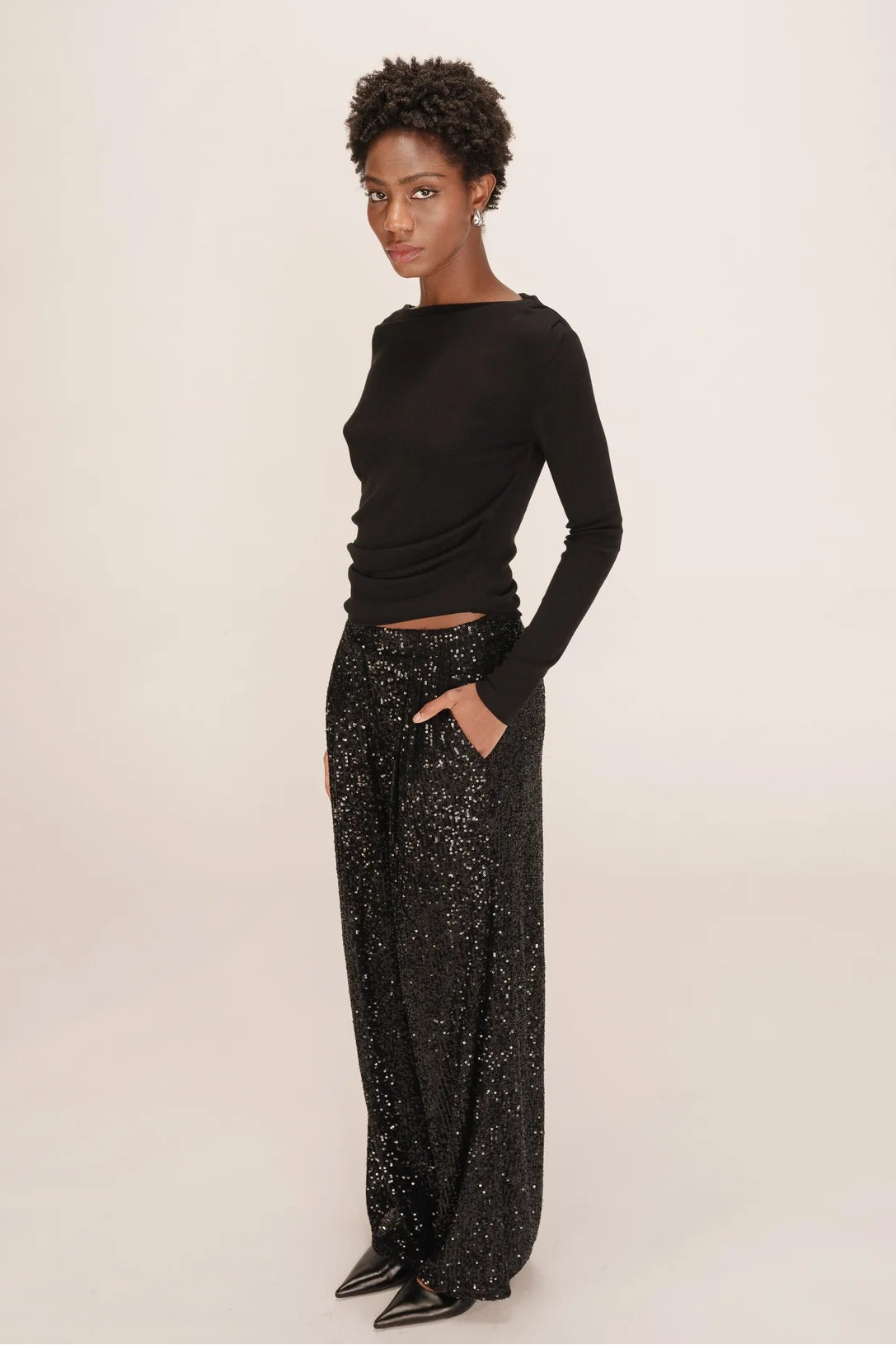 Person wearing a black long-sleeve top and black sequin pants on a white background