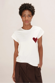 Person wearing a white t-shirt with a red heart design on a plain background
