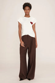 Person wearing a white t-shirt with a red heart design and brown pants on a plain background
