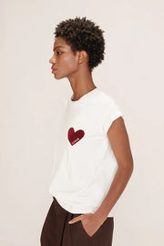 Person wearing a white t-shirt with a red heart design on a plain background