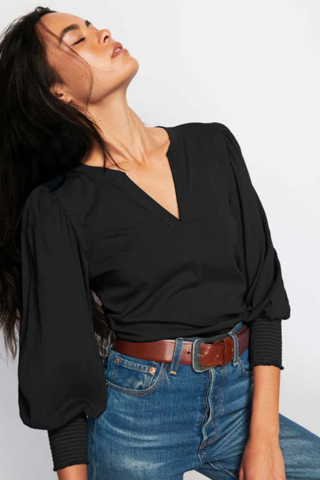 Woman wearing a black top and blue jeans against a light gray background