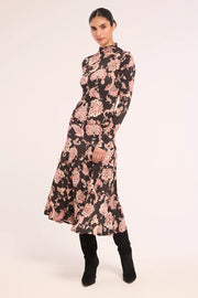 A woman models a long-sleeved midi dress with a black base and a pink floral paisley pattern, paired with black boots, against a plain light background.