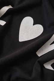 Woman wearing wearing a black crewneck t-shirt with the word "LOVE" written on the front in white lettering, fabric detail view