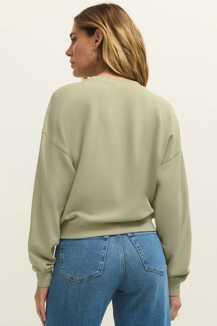 Woman wearing a sage green long sleeve sweatshirt with the word "Ciao" written on the front in yellow back view
