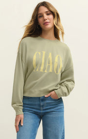 Woman wearing a sage green long sleeve sweatshirt with the word "Ciao" written on the front in yellow front view