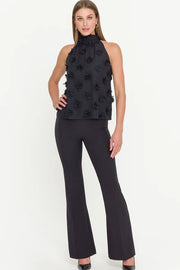 woman wearing a halterneck black top with 3D fabric flowers all over with black dress pants
