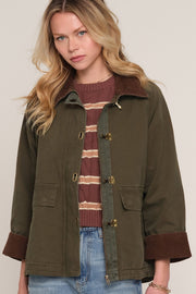 A woman wearing an olive green utility jacket with brown corduroy collar and cuffs, 