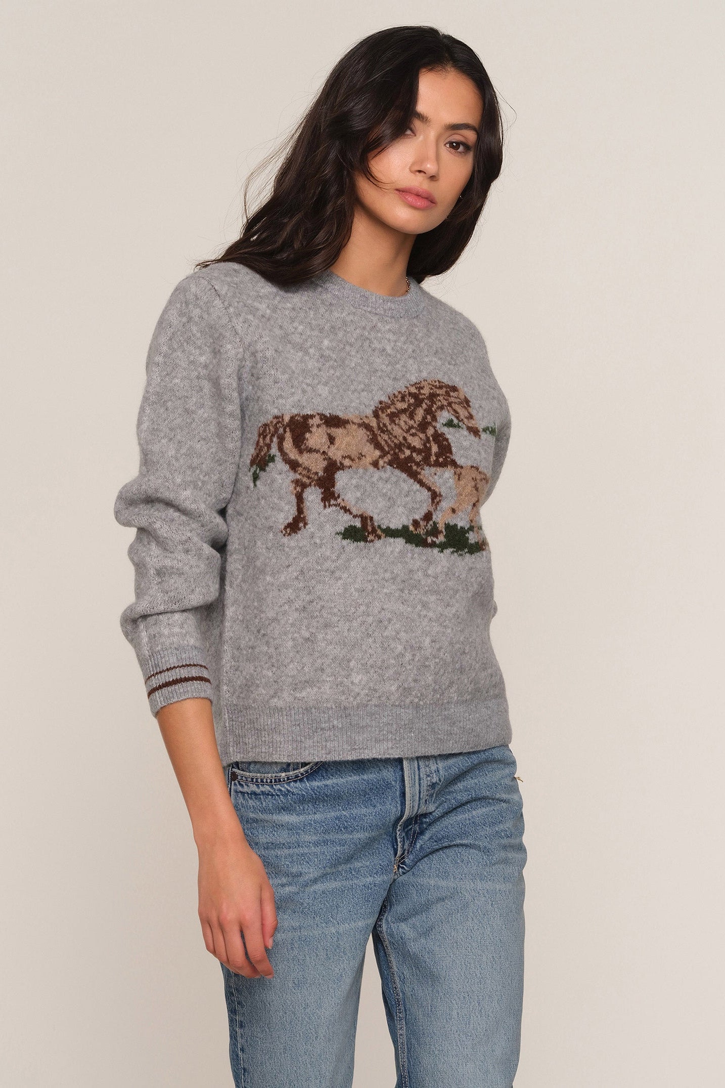 A woman wearing a heather gray crewneck sweater with a large brown horse graphic across the chest