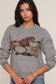 A woman wearing a heather gray crewneck sweater with a large brown and beige horse and foal graphic across the chest