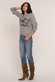 A woman modeling a heather gray crewneck sweater with a brown and beige embroidered horse design on the front