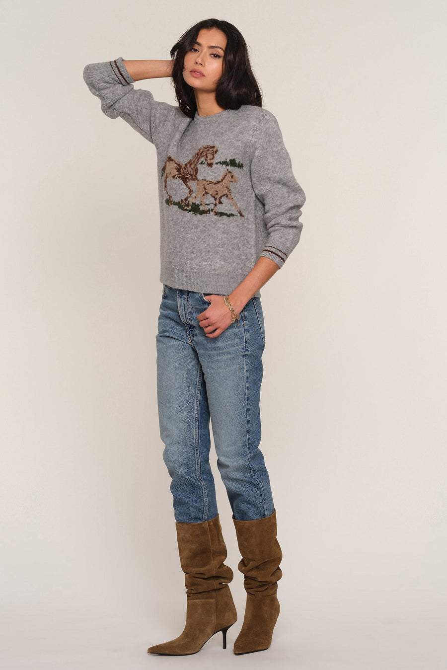 A woman modeling a heather gray crewneck sweater with a brown and beige embroidered horse design on the front