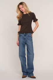 A woman modeling a dark brown short-sleeve knit top with ruffled sleeves and raw hems