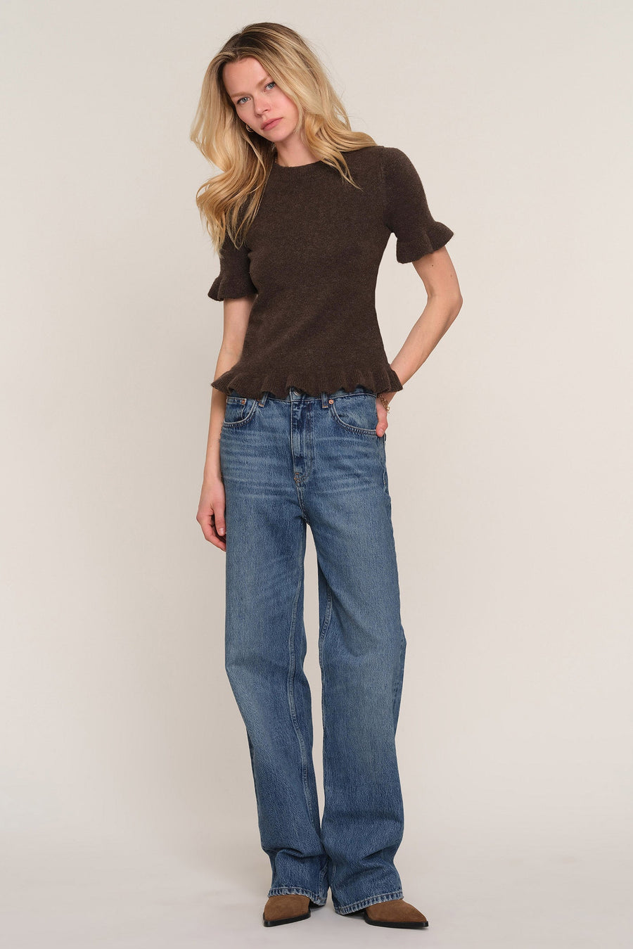 A woman modeling a dark brown short-sleeve knit top with ruffled sleeves and raw hems