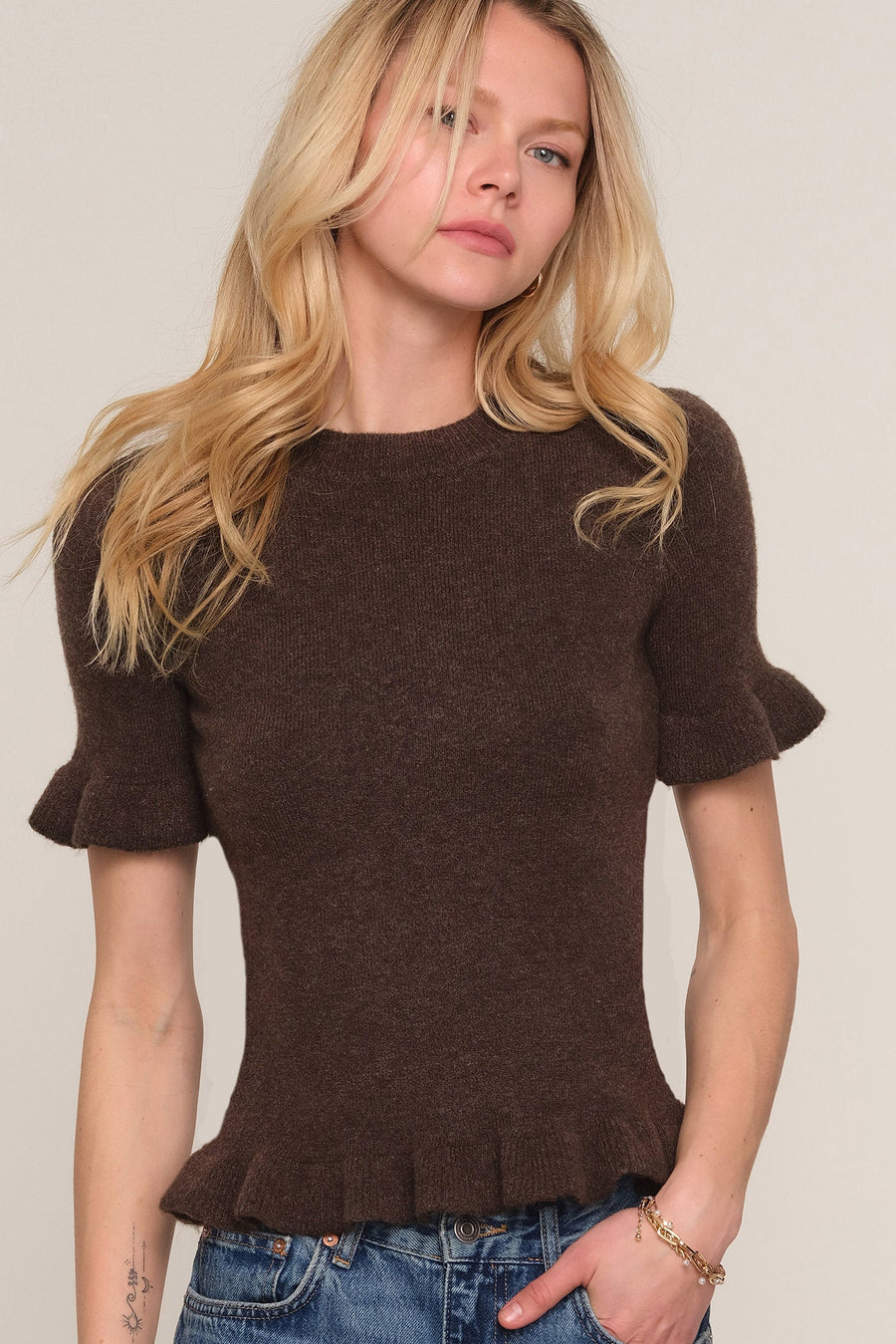 A woman wearing a dark brown short-sleeve knit top with ruffled cuffs and a ruffled hem