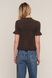 A woman viewed from the back wearing a short-sleeve brown knit top with ruffled cuffs and a ruffled hem