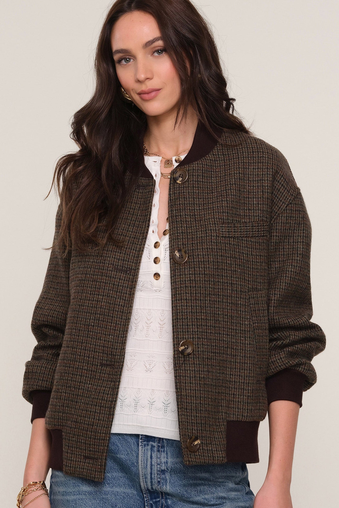 Front view of a person wearing an open brown checkered bomber jacket and blue jeans