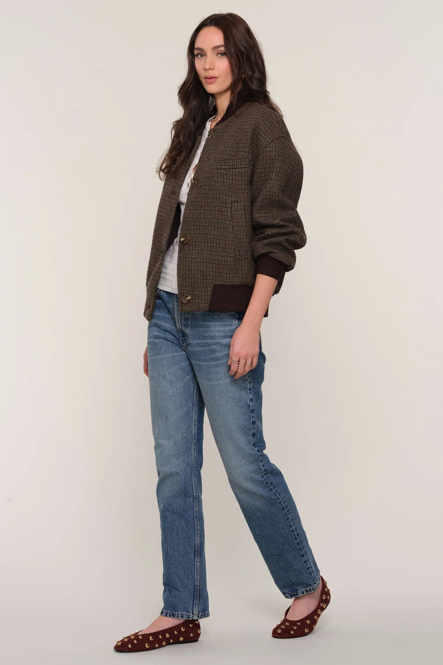 3/4 view of a person wearing a brown checkered bomber jacket and blue jeans