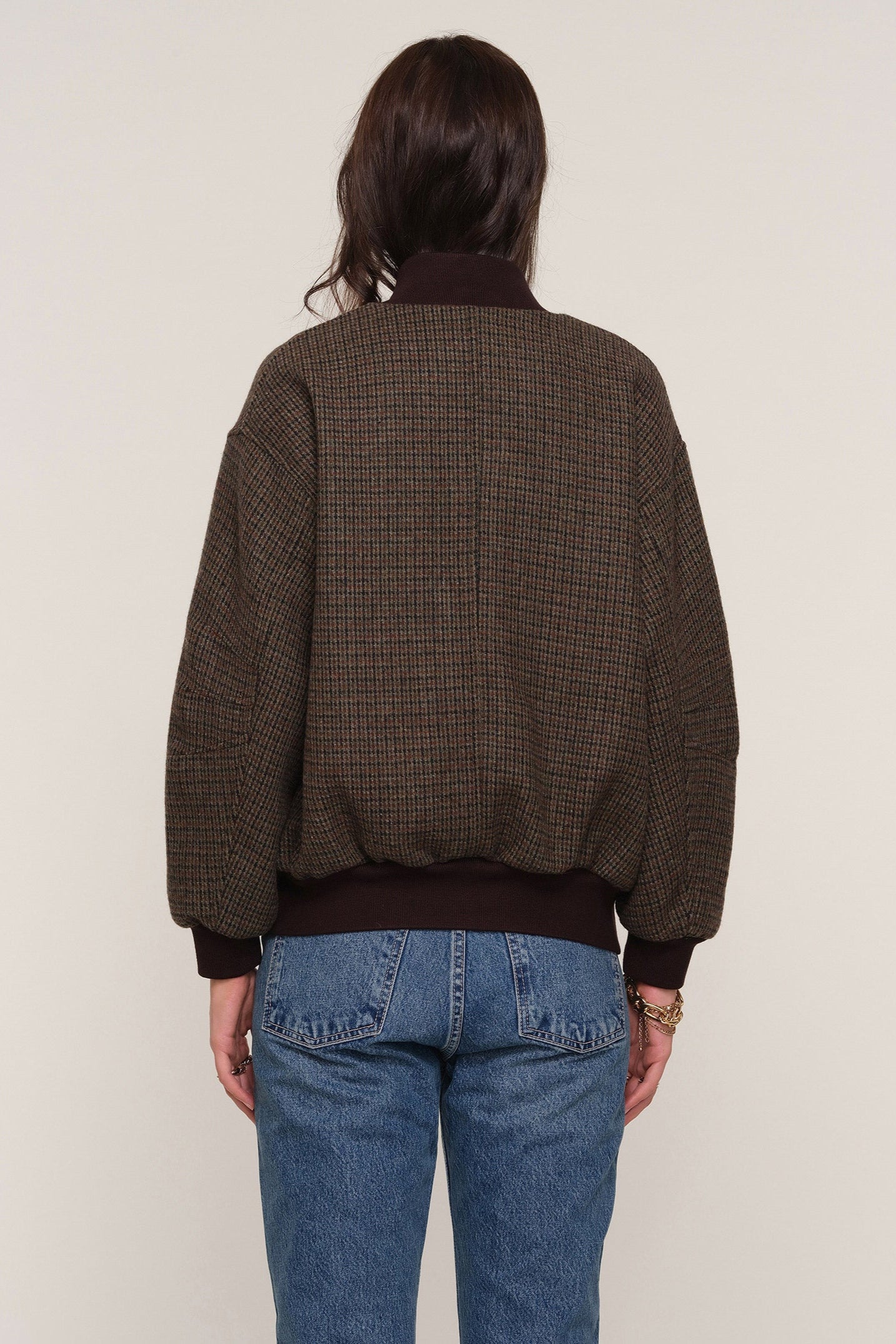 Back view of a person wearing a brown checkered bomber jacket and blue jeans