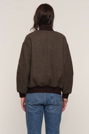 Back view of a person wearing a brown checkered bomber jacket and blue jeans
