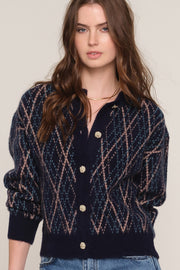 A woman wearing a navy blue knit cardigan with a beige and white diamond pattern, featuring gold buttons