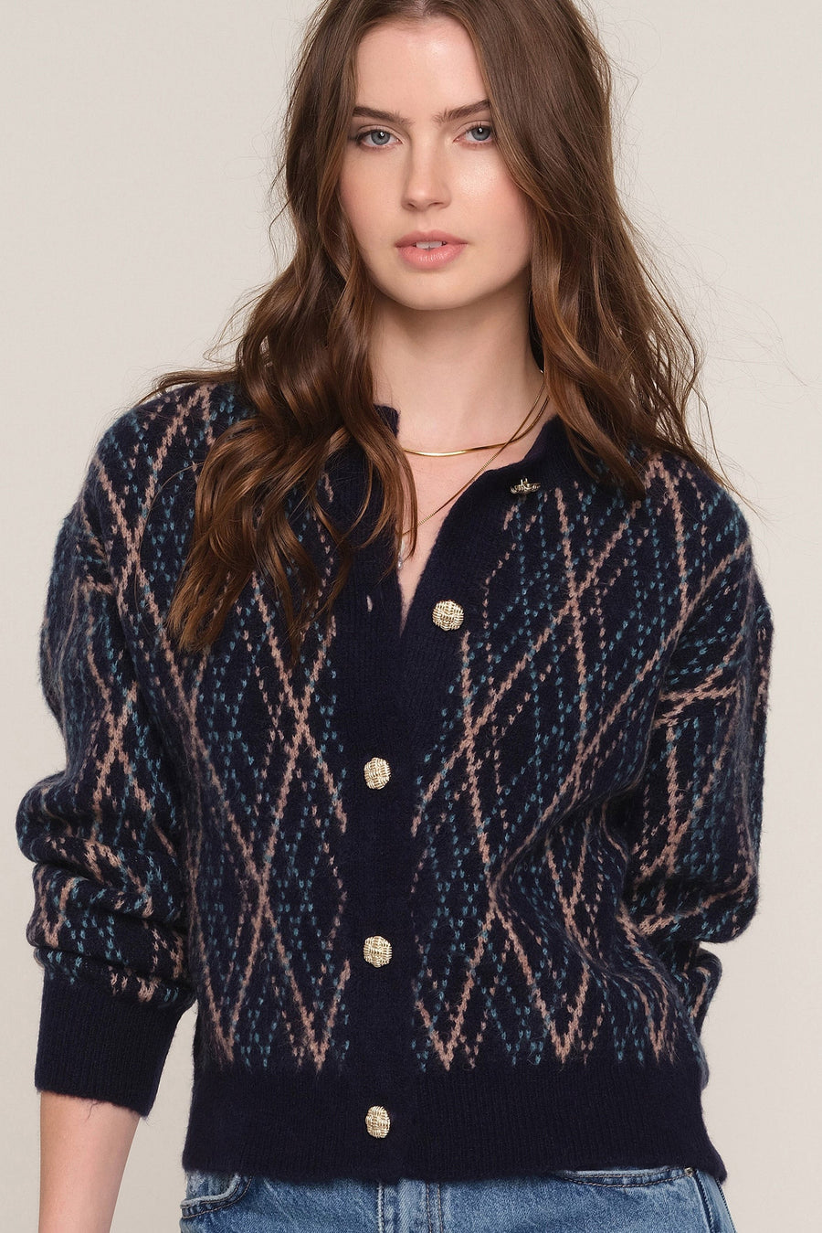 A woman wearing a navy blue knit cardigan with a beige and white diamond pattern, featuring gold buttons