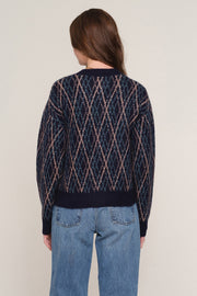 A woman viewed from the back wearing a navy blue knit sweater with a pink and beige diamond argyle pattern