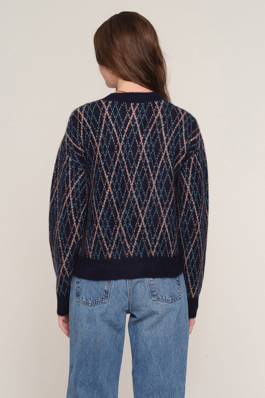 A woman viewed from the back wearing a navy blue knit sweater with a pink and beige diamond argyle pattern