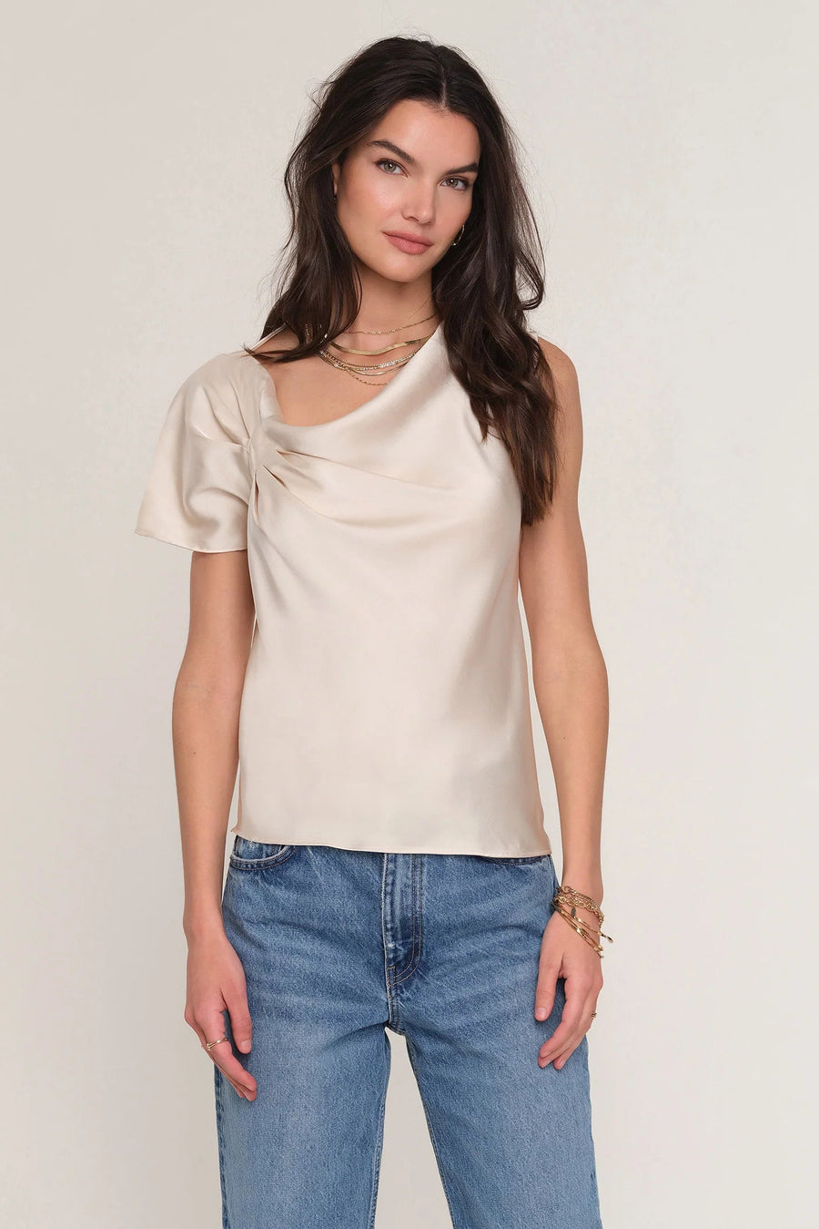 Woman wearing a satin cream top with draped neckline. 