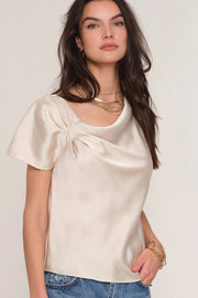 Woman wearing a satin cream top with draped neckline. 