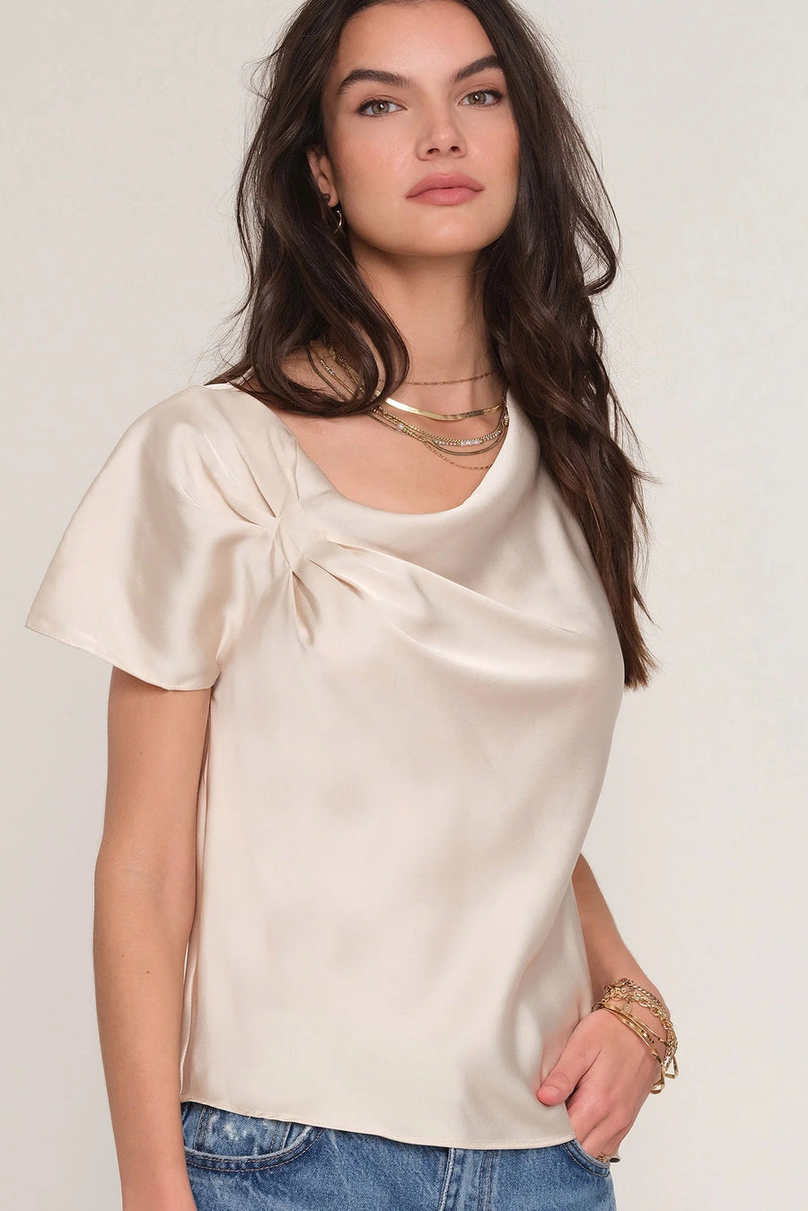 Woman wearing a satin cream top with draped neckline. 