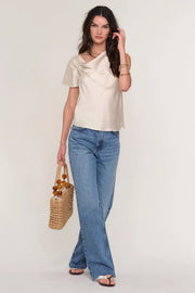 Woman wearing a satin cream top with draped neckline. 