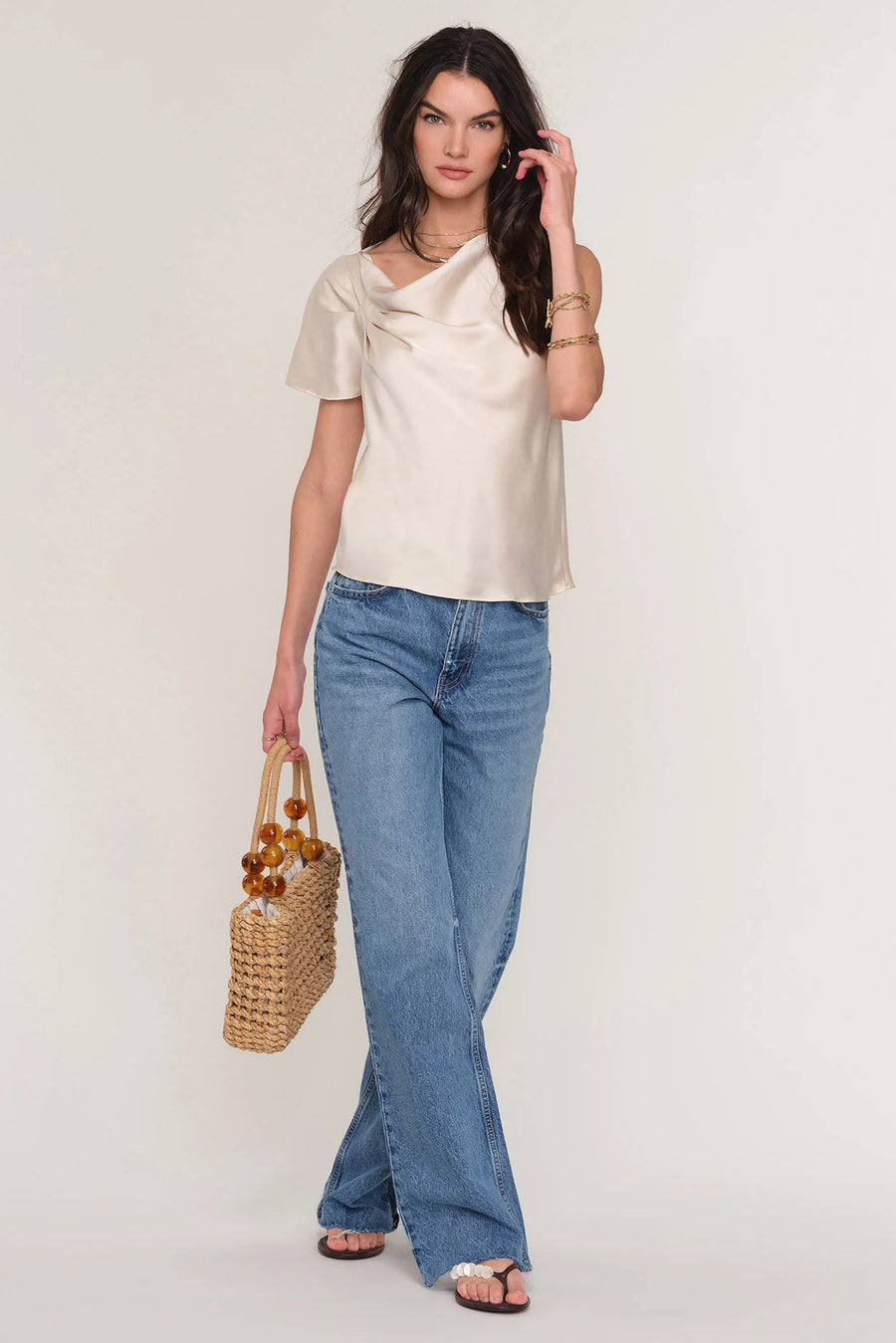 Woman wearing a satin cream top with draped neckline. 