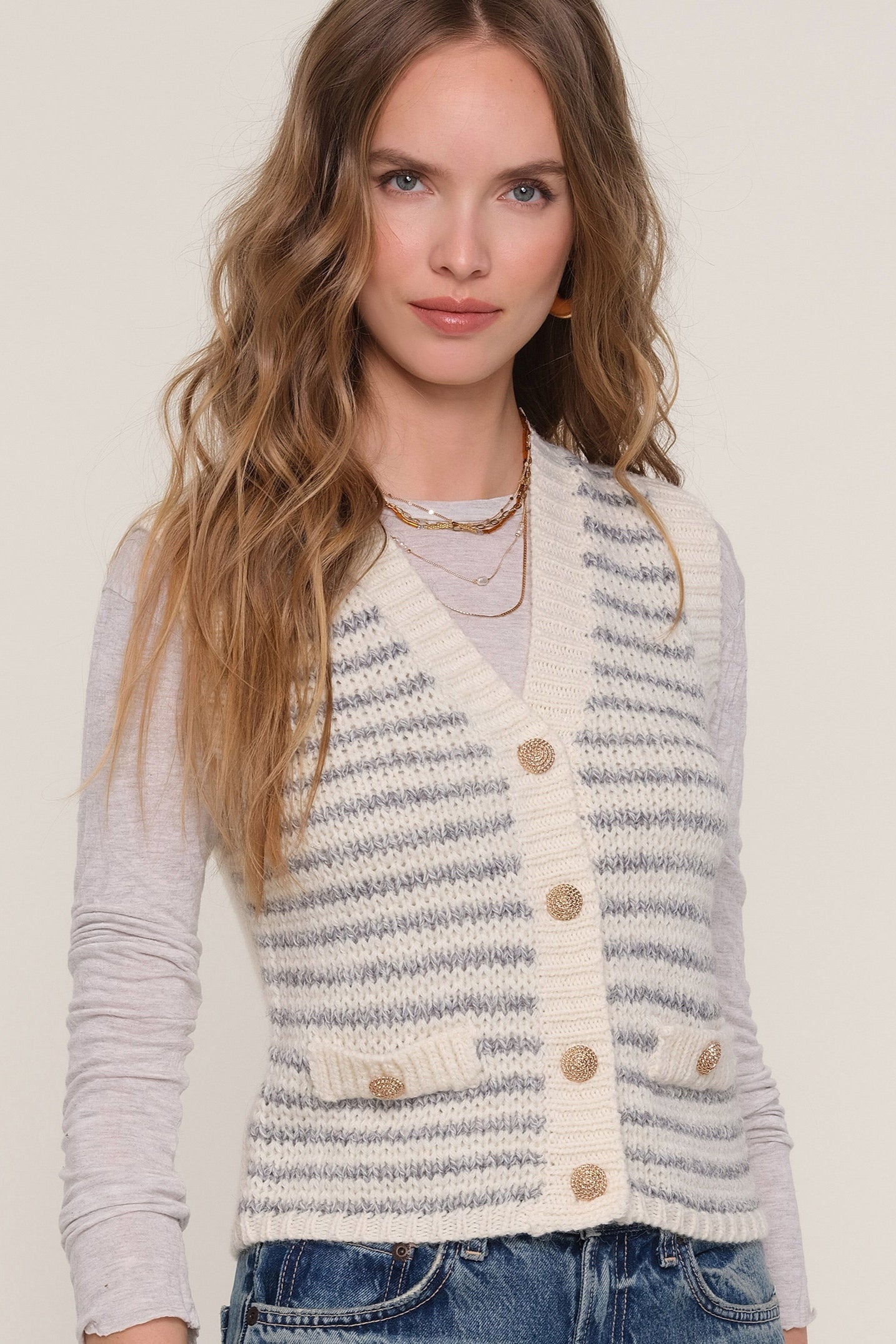 Close-up view of woman wearing a blue and white striped knit vest with gold hardware