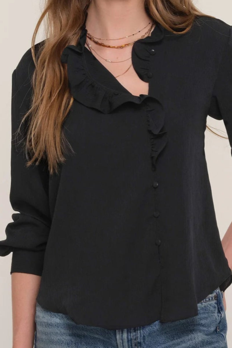 Close-up of a woman wearing a black blouse with ruffles and blue jeans 