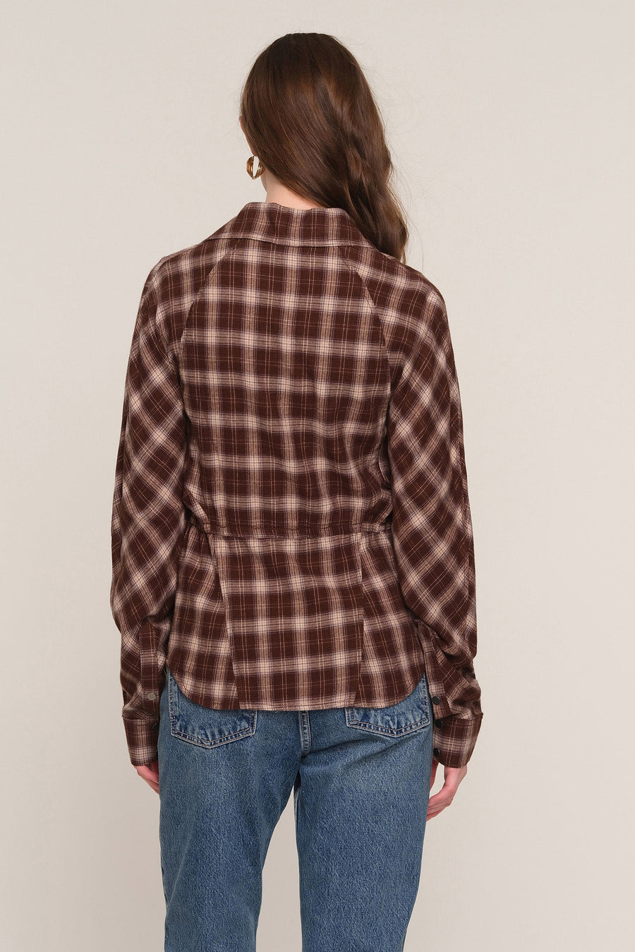 A woman viewed from the back wearing a brown and beige plaid long-sleeve shirt with a peplum waist, 