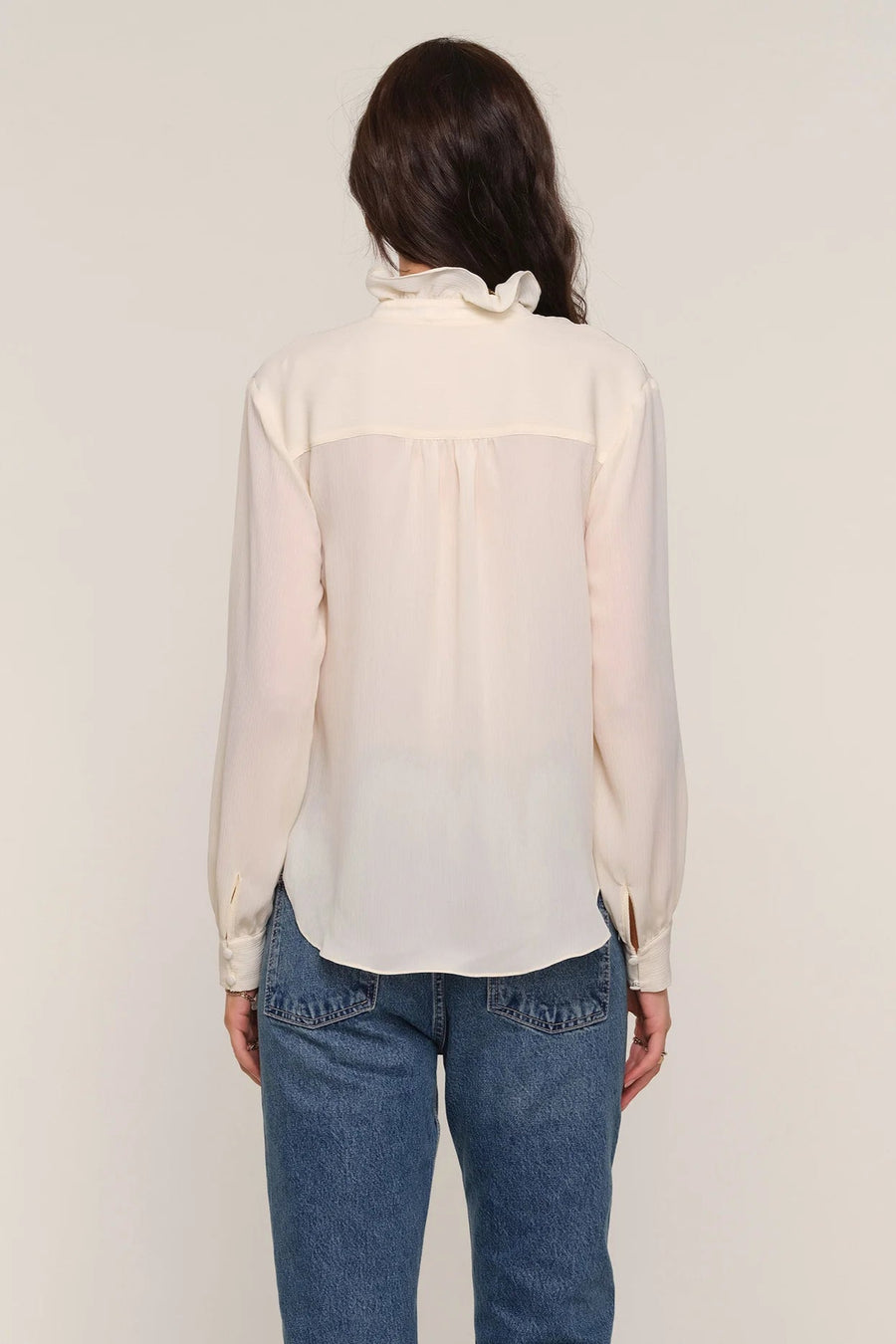 Back view of a woman wearing a cream blouse and blue jeans 